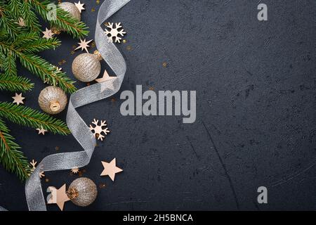 Decorazione di Natale. Decorazioni per le vacanze con baubles, rami di abete e presenti su sfondo nero scuro. Design del bordo. Vista dall'alto. Foto Stock