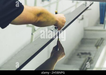 Un dipendente di una vetreria taglia una grande lastra di vetro con l'aiuto di utensili specializzati Foto Stock