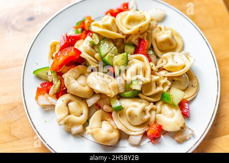 Insalata di pasta ripiena di tortellini al tavolo sopra la vista dall'alto con cetrioli a fette, peperoni rossi e condimento su piatto bianco come cibo sano Foto Stock