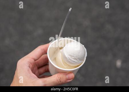 Gelato al cocco in una tazza di carta bianca in una mano Foto Stock