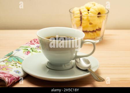 Una tazza di caffè e una ciotola di vetro con biscotti di burteria e un tovagliolo a motivi floreali su una superficie di legno. Foto Stock