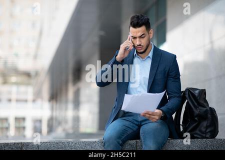 Serio uomo d'affari medio-orientale che ha conversazione telefonica per strada Foto Stock