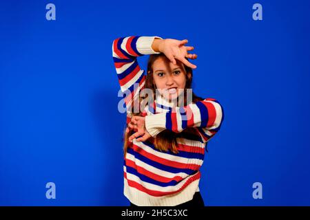 Divertente Tiger. Ritratto di simpatica bambina giocosa vestita in un maglione a righe che mostra artigli, sfondo blu studio Foto Stock