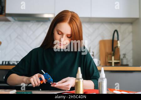 Vista frontale di attraente giovane donna incollando buste a bordo con regali per i bambini che fanno Natale calendario avvento a casa. Foto Stock