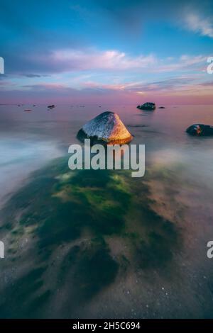 Gruppo di piccole formazioni rocciose e un colorato cielo al tramonto sul tranquillo Mar Baltico in Lituania Foto Stock