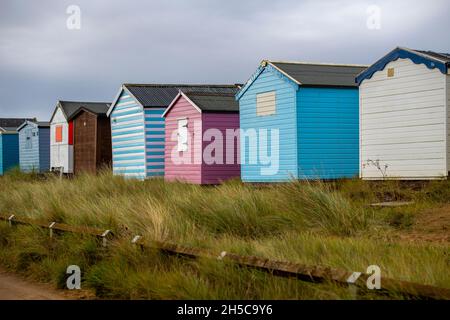 fila di capanne colorate sulla spiaggia a heacham sulla costa nord del norfolk, capanne di spiaggia dipinte in modo luminoso in una fila o linea a heacham. Foto Stock