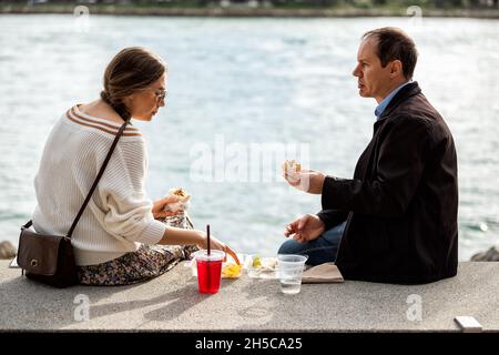 Miami Beach, USA - 17 gennaio 2021: Parco South Pointe con due candidi persone sedute a Bay Water a Miami, Florida, che mangiano sandwich e cibo per il pranzo Foto Stock