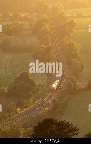 Treno che viaggia attraverso la campagna inglese, Surrey, luce notturna, punto panoramico alto, linea North Downs. Luce del sole sulle rotaie Foto Stock