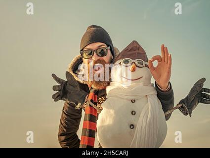 Uomo d'inverno con pupazzo di neve in cappello pilota. Uomo di Natale con barba sul volto felice. Snowman pilota, festa invernale. Foto Stock