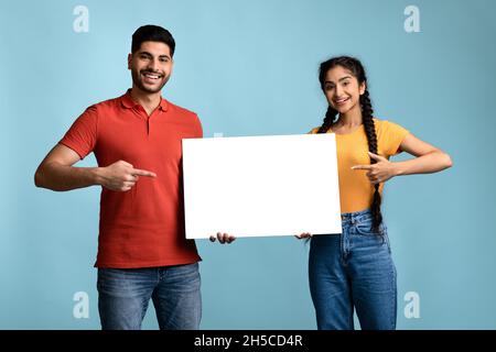 Bella offerta. Allegra coppia araba che punta in mano al Placard bianco bianco Foto Stock