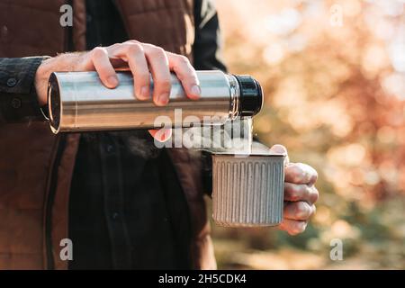 Primo piano delle mani maschili versando il tè da una bottiglia metallica sottovuoto alla tazza Foto Stock