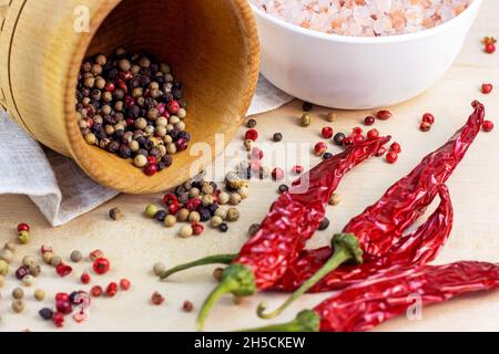 Mescolare i grani di pepe secco nel mortaio di legno e il peperoncino secco per cucinare su sfondo chiaro in cucina. Foto Stock