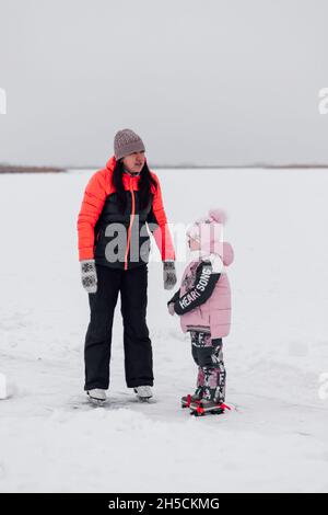 Passeggiata invernale nella natura. Giovane donna e bambina pattinare sul fiume ghiacciato, mamma e figlia Foto Stock