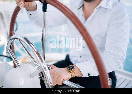Mani dell'uomo in camicia bianca seduta al timone su uno yacht che naviga in mezzo al mare, da vicino Foto Stock