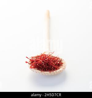 Primo piano di un cucchiaio di legno riempito di zafferano su sfondo bianco. Foto Stock