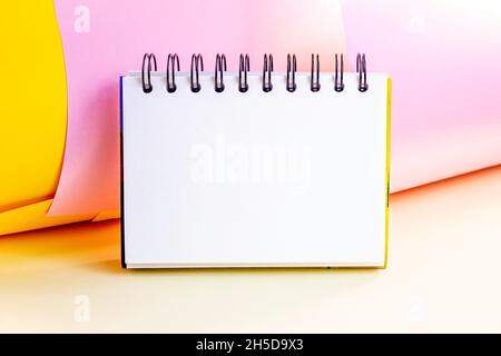 Bianco copybook da ufficio vuoto con spirale mock up per note e messaggi su sfondo luminoso e colorato. Modello di pagina del blocco note vuoto con spazio di copia Foto Stock