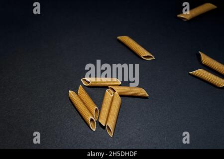 Primo piano di pasta penne non cotta su una superficie scura Foto Stock