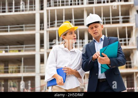 Due giovani architetti di successo sul cantiere, discutono del piano di costruzione Foto Stock