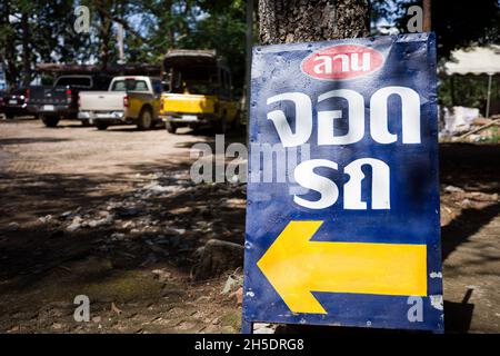 Il cartello blu della strada in lingua thailandese significa area parcheggio con freccia gialla a sinistra e sfondo sfocato delle auto da parcheggio. Foto Stock