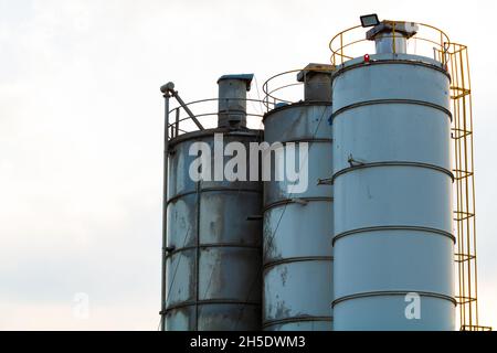 Silos di cantiere. Torri di stoccaggio isolate su sfondo cielo nuvoloso. Foto di sfondo dell'area di costruzione. Depositi di cemento. Foto Stock