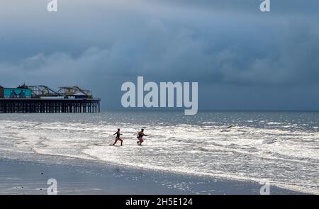 Brighton UK 19 novembre 2021 - nuotatori godersi la bassa marea sulla spiaggia di Brighton in una mattinata sovrastante lungo la costa meridionale con l'occasionale esplosione di sole attraverso le nuvole scure : Credit Simon Dack / Alamy Live News Foto Stock