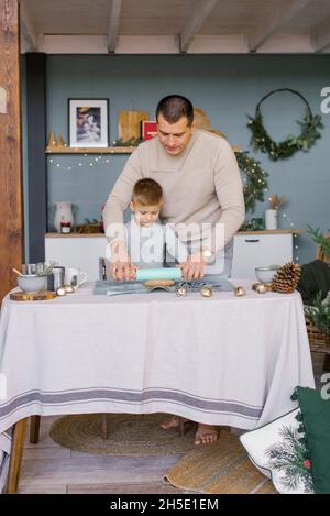 Papà e figlio tirano fuori l'impasto in cucina per i biscotti di zenzero di Natale o la casa di pan di zenzero Foto Stock