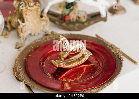 Cavallo d'oro souvenir di Natale su un piatto rosso e oro. Servizio e arredamento della cena festiva di Capodanno Foto Stock