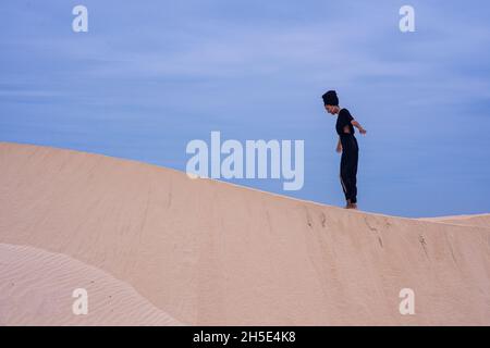 Donna che cammina lungo la duna di sabbia con cielo limpido Foto Stock