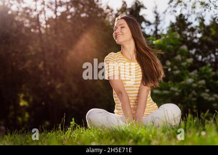 Ritratto di attraente ragazza allegra seduta su erba passare tempo libero riposo vacanza sole splendente luminoso all'aperto Foto Stock