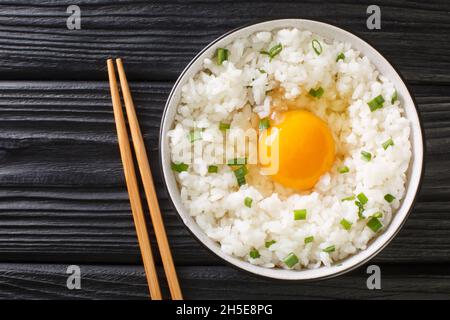 Tamago kake gohan è un piatto giapponese semplice fatto di uova crude su riso da vicino nella ciotola sul tavolo. Vista dall'alto orizzontale Foto Stock