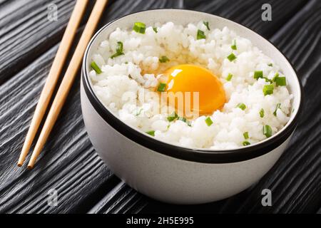 Tamago kake gohan è un piatto giapponese semplice fatto di uova crude su riso da vicino nella ciotola sul tavolo. Orizzontale Foto Stock