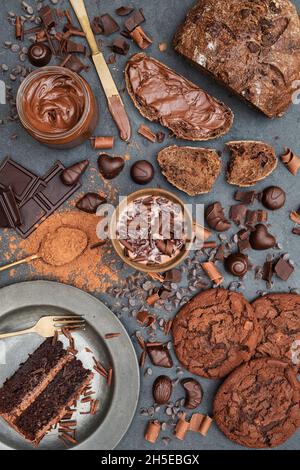 Pasta al cioccolato, biscotti al cioccolato, torta al cioccolato, cioccolata calda, cacao con pasta alle nocciole, barra al cioccolato e pezzi su sfondo ardesia Foto Stock