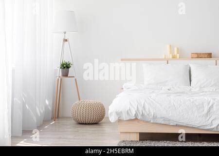 Grande letto matrimoniale con biancheria da letto confortevole, lampada in camera da letto, moquette grigia, ottomana, mobili con accessori Foto Stock