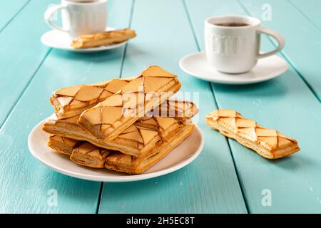 Panetteria italiana croccante Sfogliatina vetro su un piattino e due tazze di caffè caldo su tavola di legno turchese. Colazione dolce con pasticcini a base di pasta sfoglia. Foto Stock