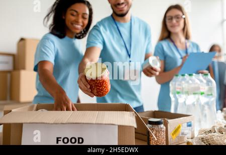 I volontari millennial mettono i vasi nella scatola mentre ordinano il cibo donato, lavorando nel centro di donazione di carità della Comunità Foto Stock