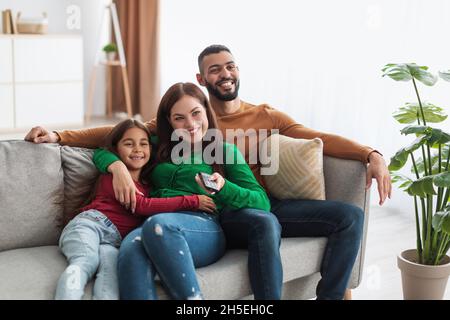 Felice giovane famiglia araba che guarda la televisione seduta sul divano Foto Stock