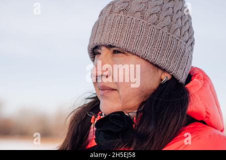 Ritratto di giovane donna. Bella brunette guarda alla foresta invernale e gode di una passeggiata nella natura dopo la nevicata, inverno gelido sole mattina Foto Stock