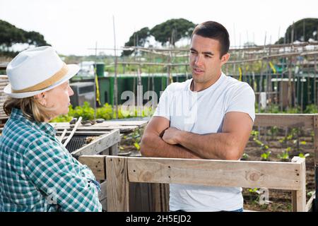 Donna anziana e giovane uomo che parla al confine della trama orto Foto Stock