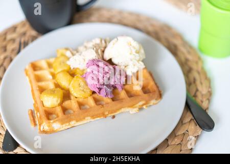 Cialde belghe dolci con frutta e gelato al limone con banane caramellate fresche su piatto bianco presso il ristorante caffetteria in estate di festa. Sano Foto Stock