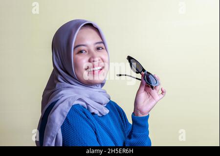 Ragazza indonesiana che indossa hijab grigio su terra gialla posteriore Foto Stock