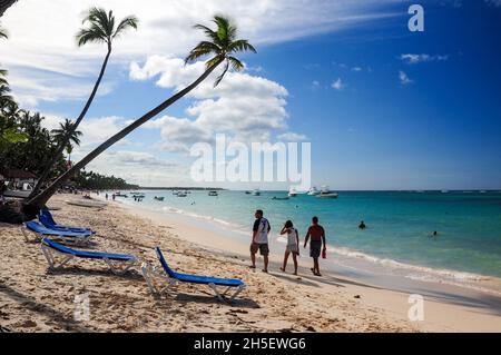 I turisti che camminano lungo la spiaggia con acque turchesi e alcune sedie a sdraio sulla sabbia a Punta Cana, Repubblica Dominicana Foto Stock