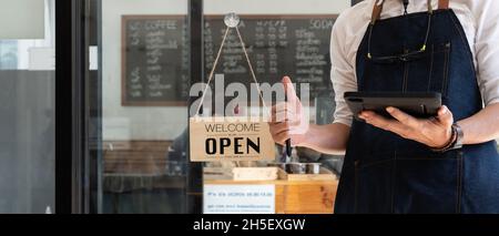 Primo piano del proprietario del negozio aprire il cartello attraverso il vetro della porta e pronto a servire. Servizio hotel, bar-ristorante, negozio al dettaglio, piccolo Foto Stock