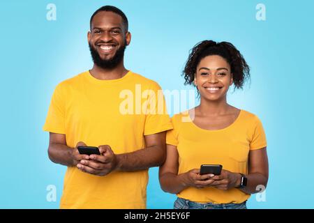 Giovane coppia nera affettuosa con telefoni cellulari, navigare in internet, controllare i social media, inviare messaggi sms Foto Stock