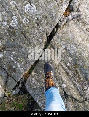 Donna che fa un passo su una scogliera nelle sue nuove scarpe invernali. Foto Stock