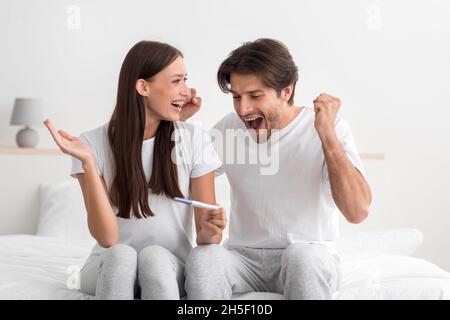 Felice emozionale giovane caucasico uomo e donna tenere test di gravidanza in camera da letto interno e gioire Foto Stock