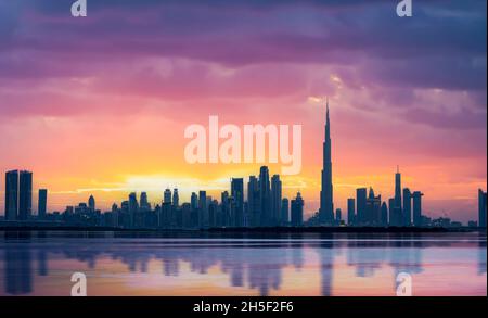 Splendida vista panoramica dello skyline di Dubai durante uno splendido tramonto con un'acqua setosa e liscia che scorre in primo piano. Foto Stock