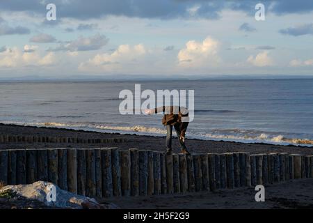 Un uomo più anziano che si bilancia, camminando su un groyne di legno su una spiaggia. Foto Stock