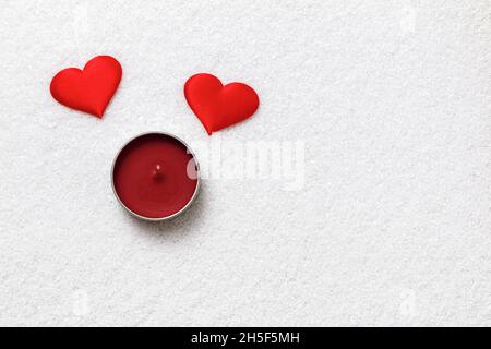 Concetto di San Valentino. Due cuori rossi e candela su neve bianca. Foto Stock