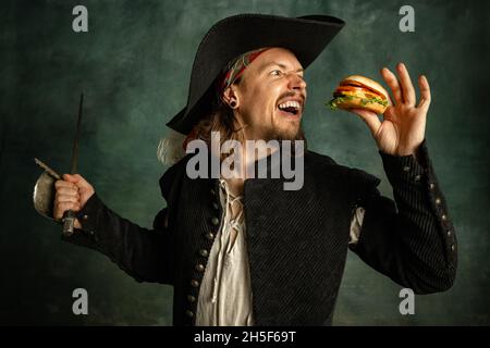 Ritratto di un uomo brutale, pirata medeival con hamburger isolato su sfondo scuro. Foto Stock