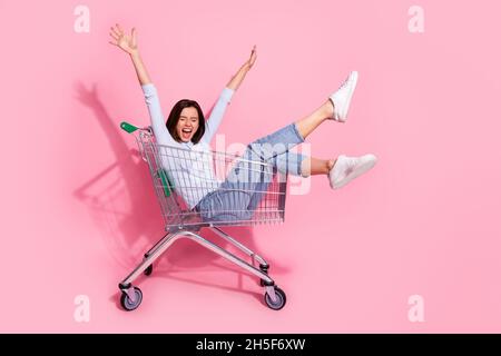 Foto di divertente eccitata giovane donna indossare maglione bianco urlando equitazione carrello sollevamento braccia sorridenti isolato rosa sfondo di colore Foto Stock